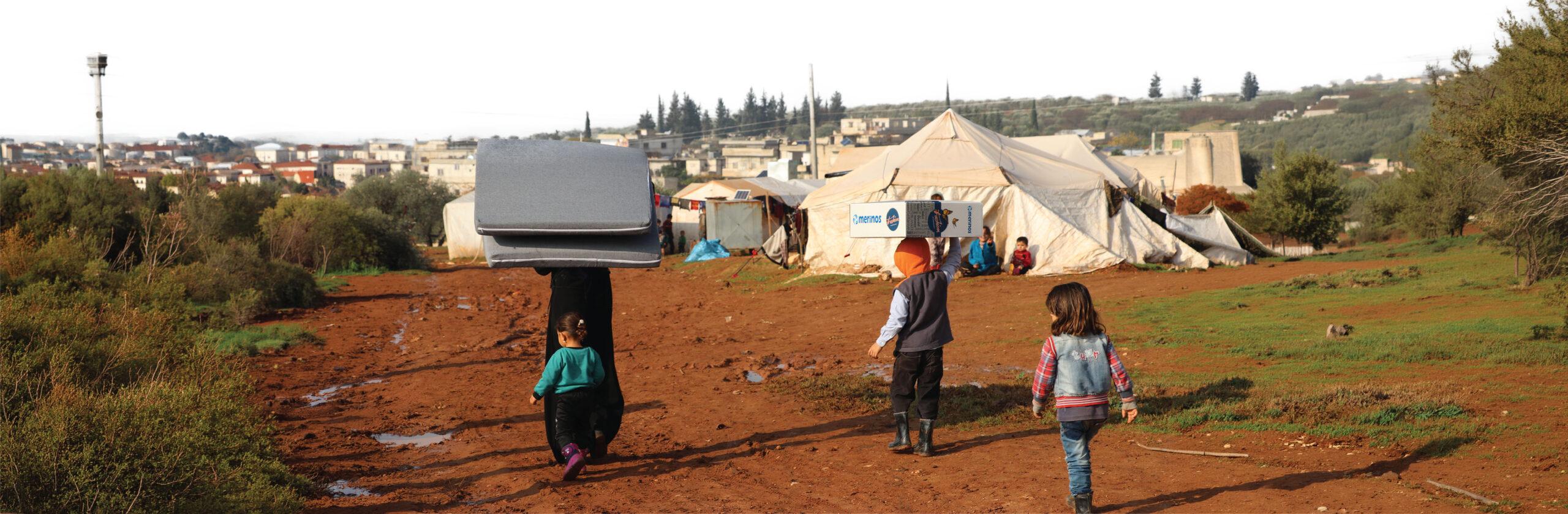 Families in a refugee camp carrying mattresses and blanket boxes delivered for winter